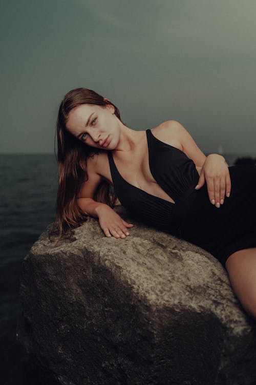 A woman laying on a rock in black swimsuit