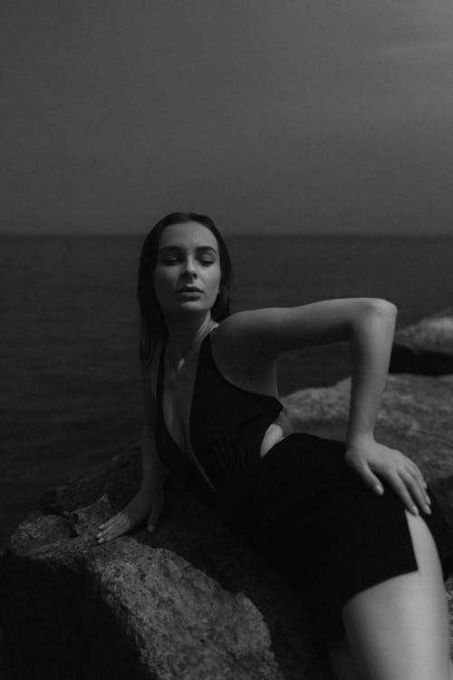 A woman in a black dress sitting on rocks by the water