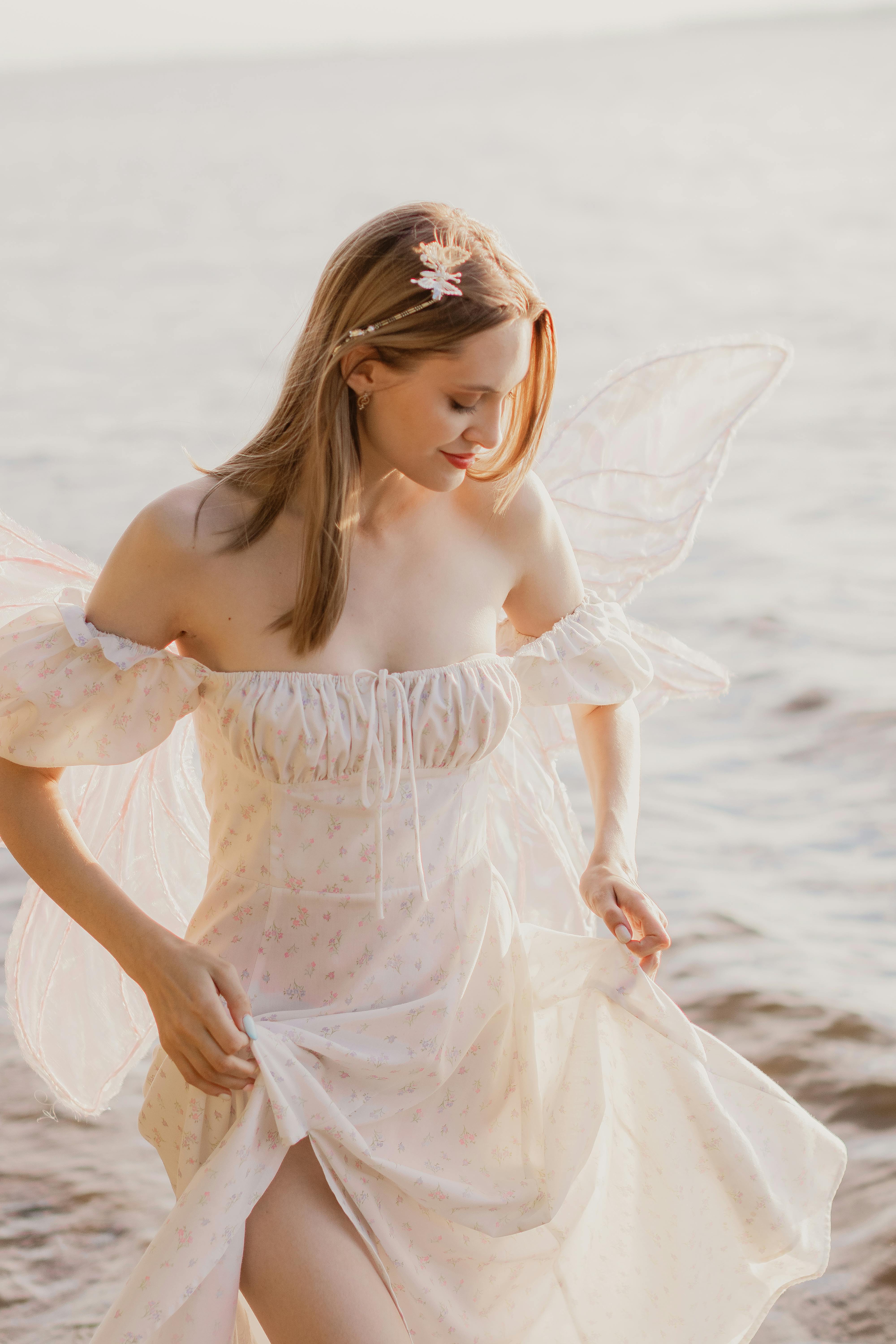 A woman dressed in a delicate fairy costume standing by the sunny seashore.