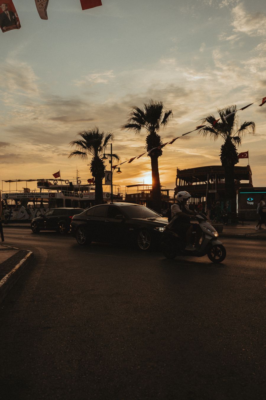 Gün batımında sahil yolunda palmiyeler ve bir motosiklet