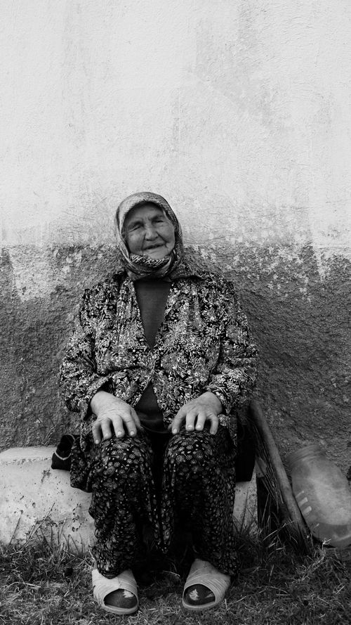 Free Black and white photo of a senior woman with headscarf sitting against a textured wall. Stock Photo