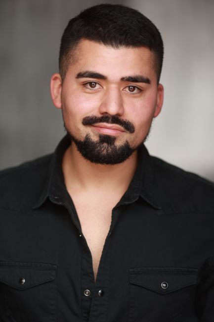 Fotomural Un hombre seguro de sí mismo con barba y bigote, sonriendo en una camisa negra sobre un fondo neutro.