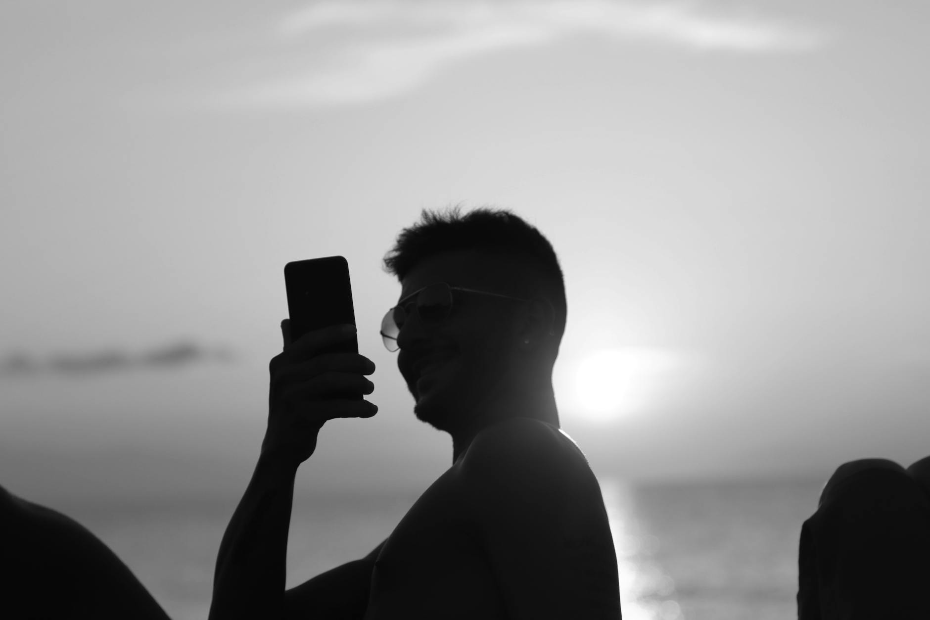 Backlit silhouette of a man using a phone at sunset on a beach in Cefalù, Sicily.