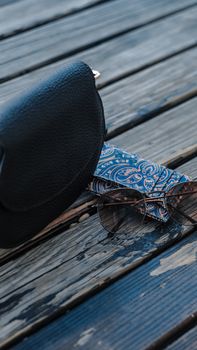 Stylish leather purse and sunglasses on a rustic wooden background for a trendy look.