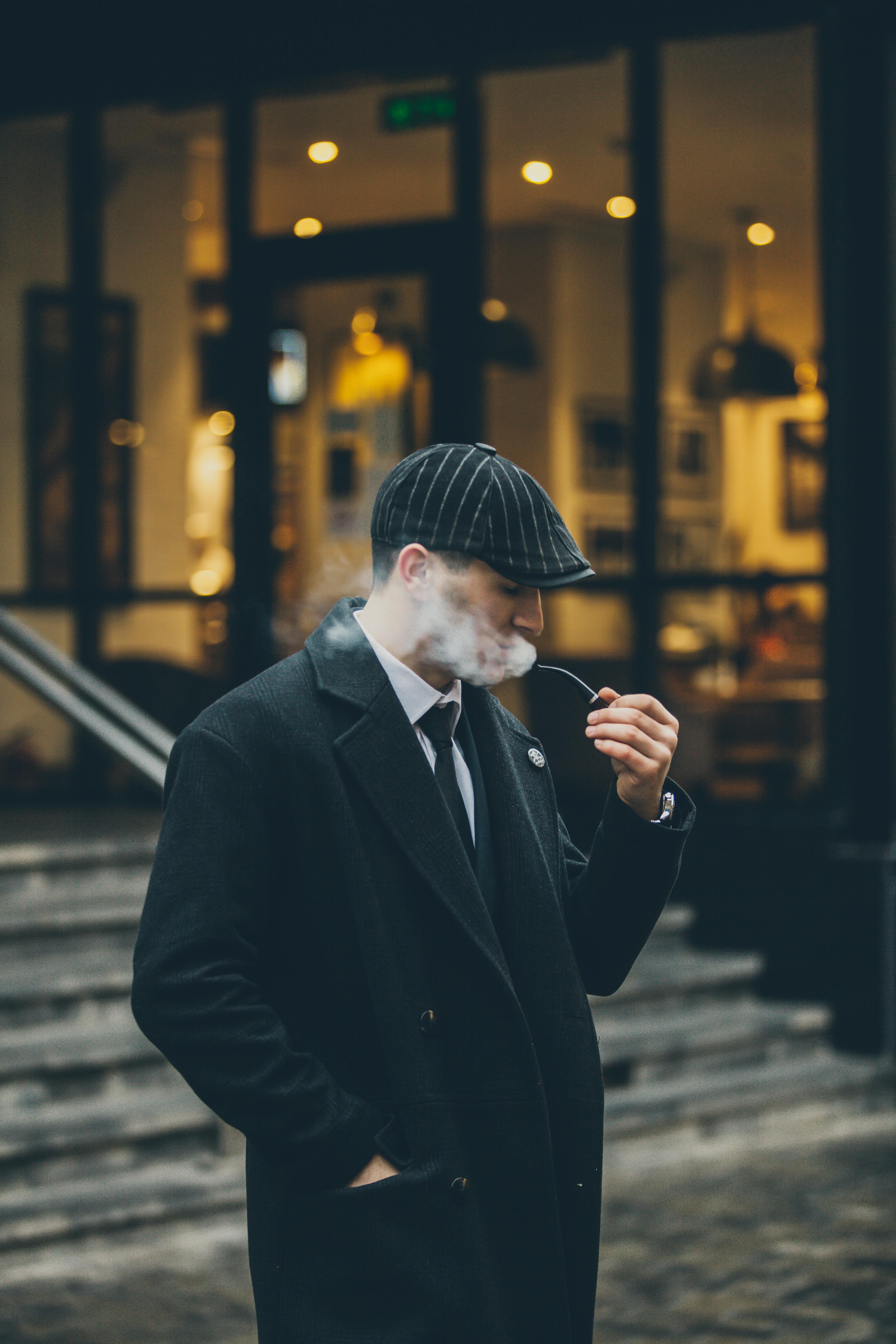 a man in a coat and peaked cap smoking a pipe