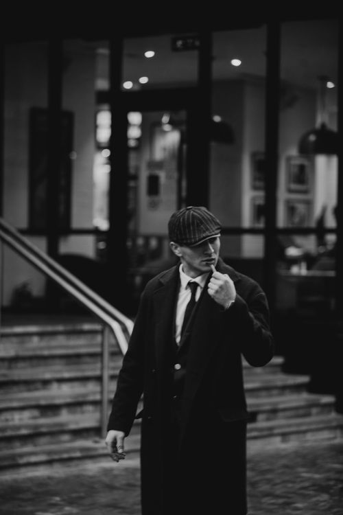 Free Vintage noir photo of an elegant man smoking on a city street, exuding mystery and style. Stock Photo