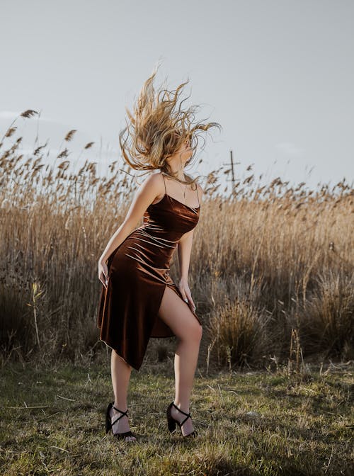 Woman in a Dress and Heels Standing on a Field and Tossing Her Hair 