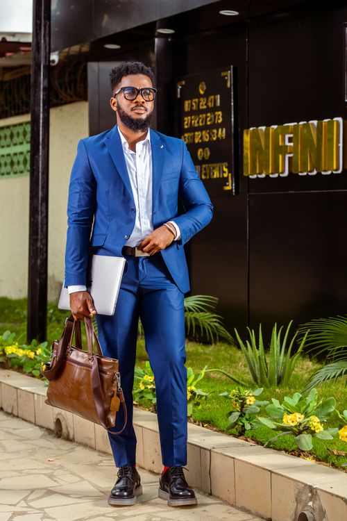 Free Businessman in a blue suit with a leather bag and laptop standing outside an office building. Stock Photo