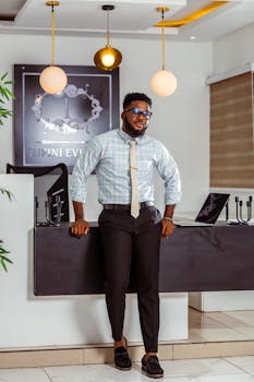 Well-dressed man in office with elegant decor, leaning on desk, exuding confidence.