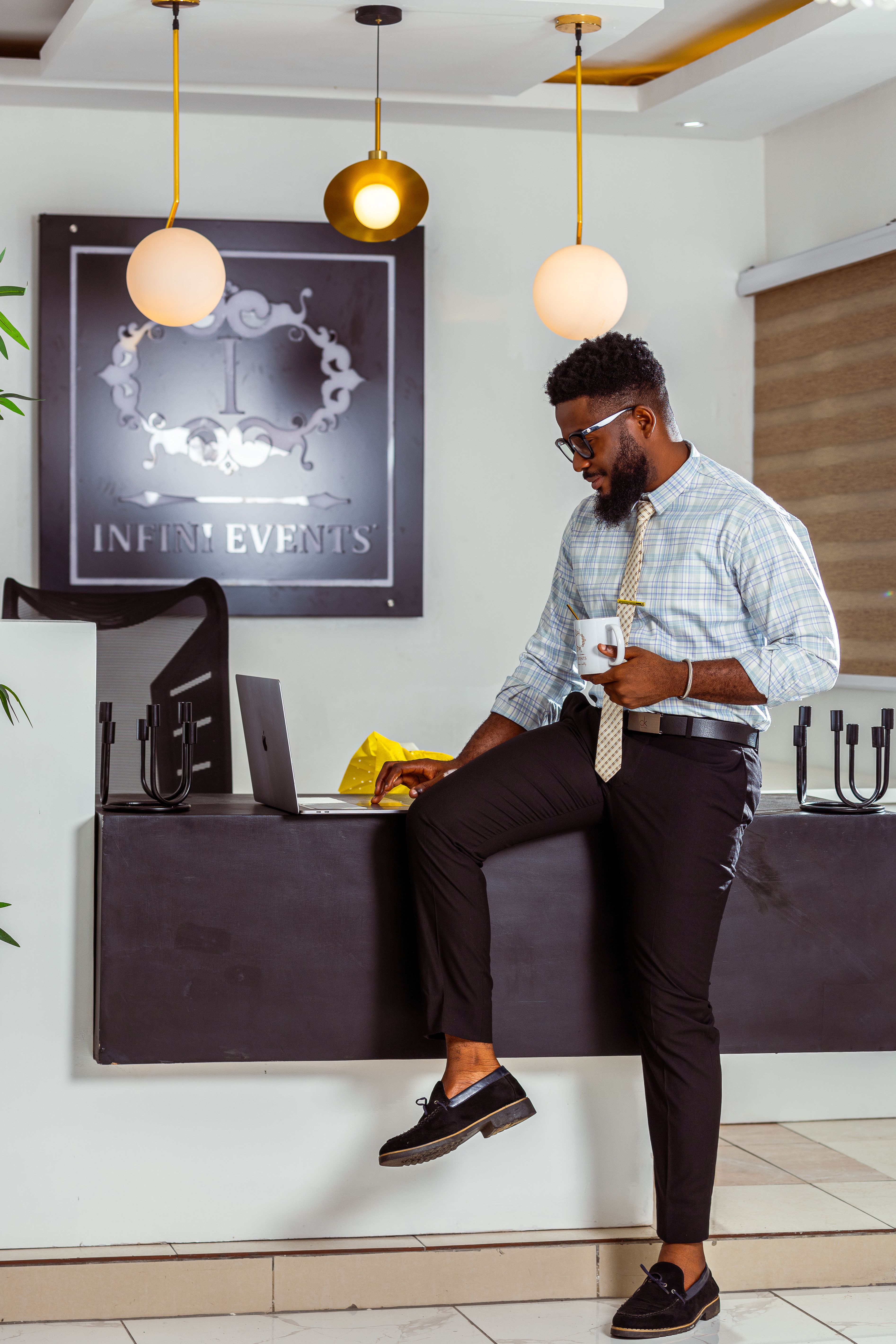 Stylish man in an office setting, working with a laptop while holding a coffee mug.