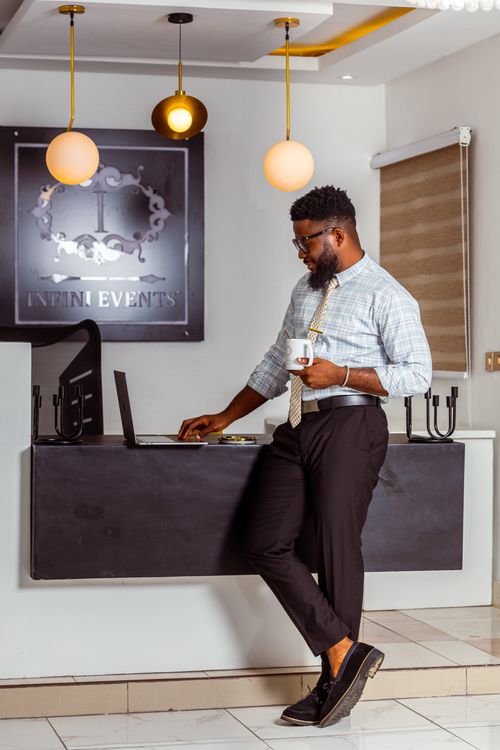 Free Well-dressed man holding coffee, using laptop in a modern office setting with elegant decor. Stock Photo