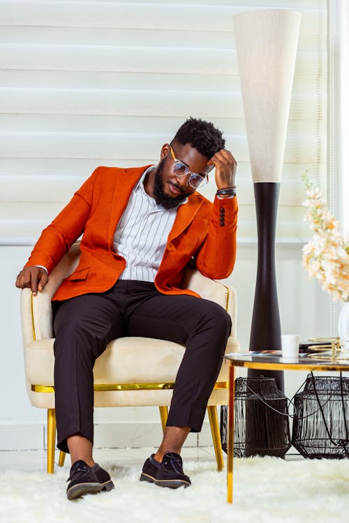 Model in a Casual Suit with a Red Jacket and Black Pants with a Crease Sitting in an Armchair