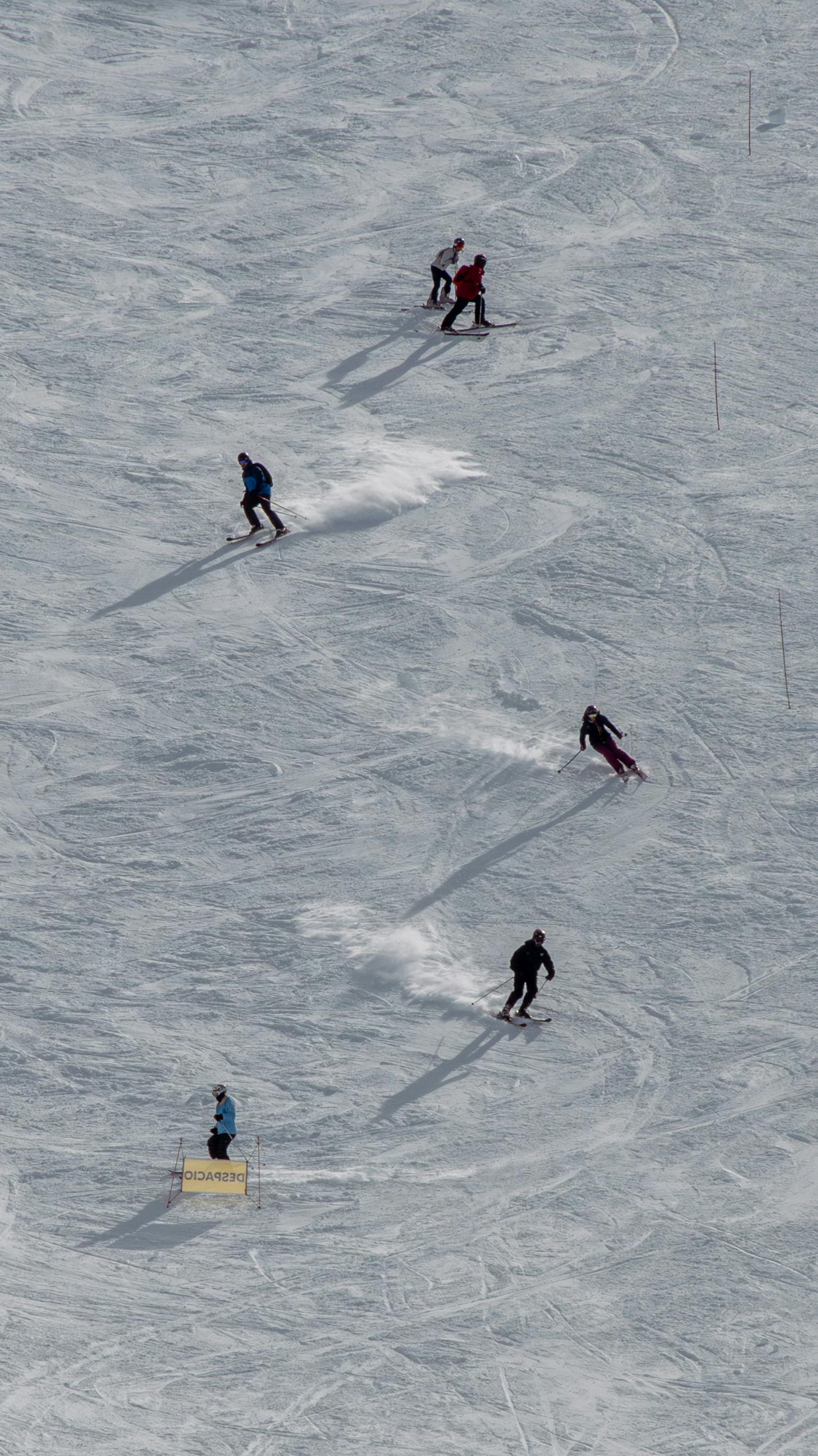 A group of skiers enjoy a thrilling descent on a snowy mountain slope under the sun.