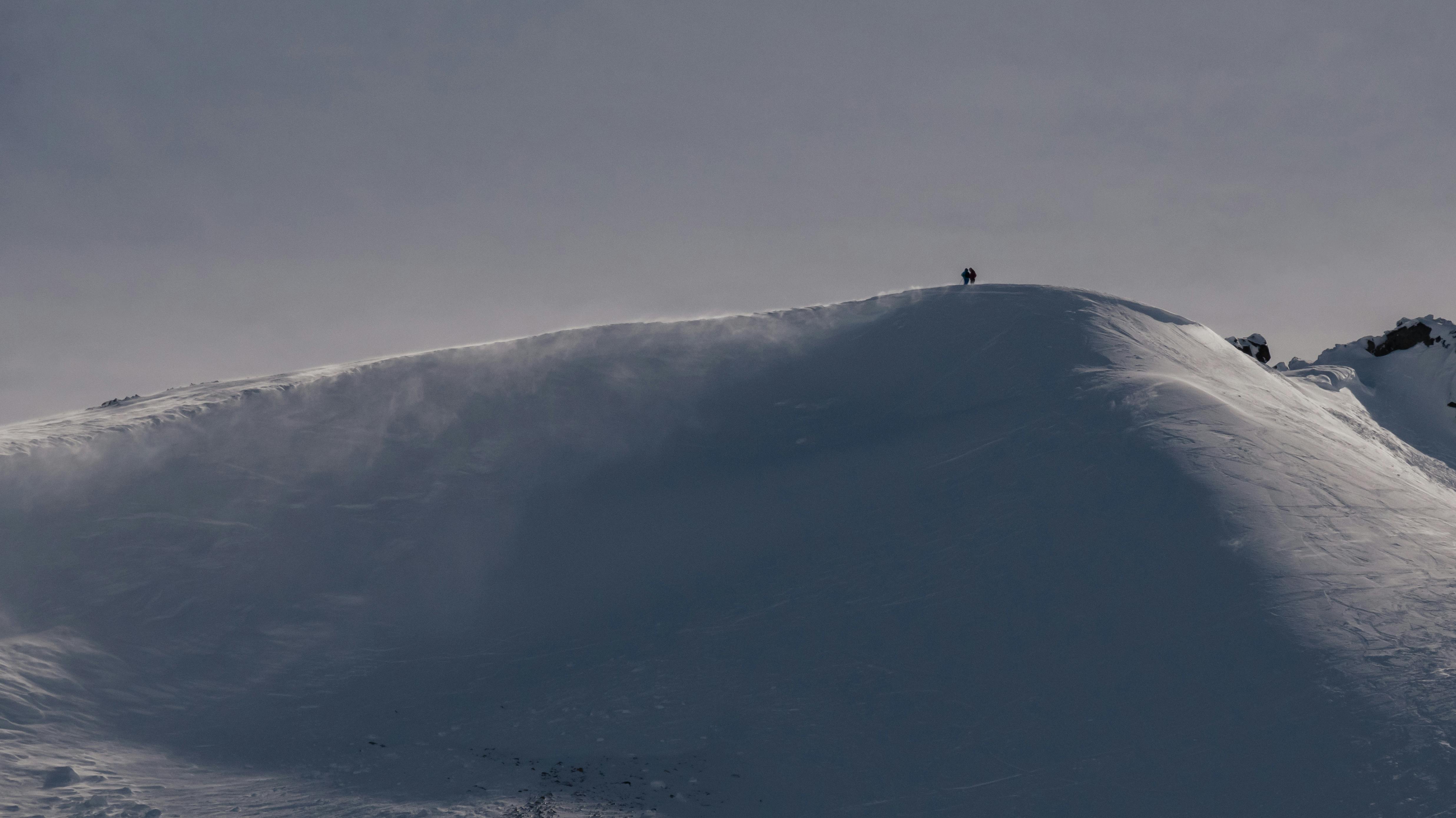 A lone skier traversing a snow-covered mountain peak under clear skies.