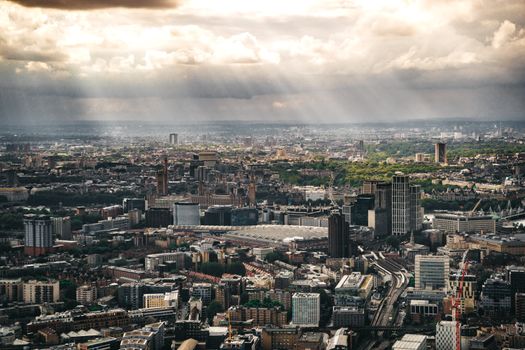 Aerial view of London's cityscape at sunset with dramatic cloud formations and sunbeams.
