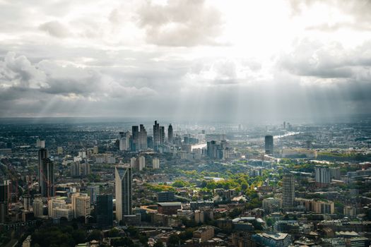 Stunning aerial view of London's cityscape under dramatic clouds and sunbeams during sunset.