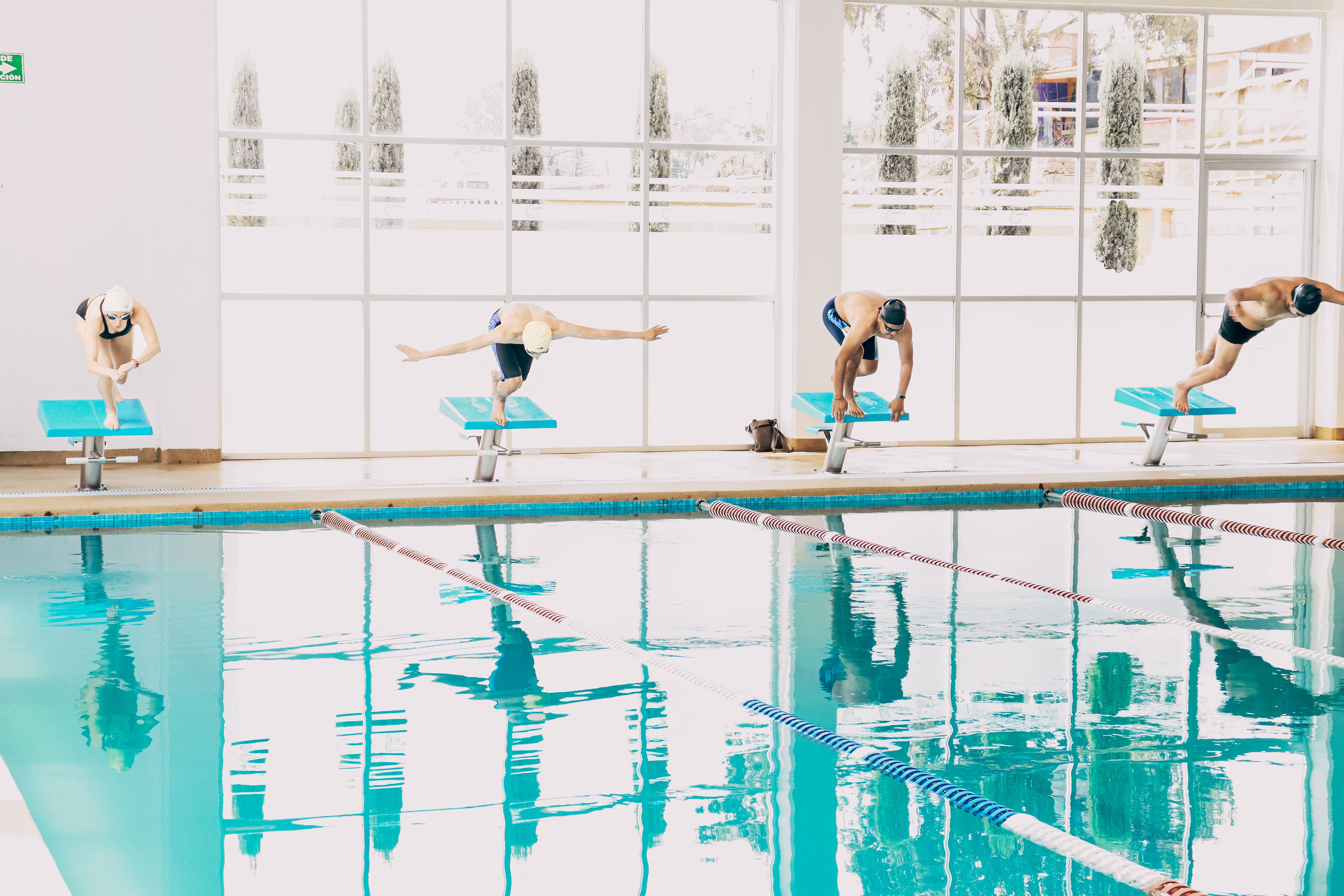 Swimmers poised on diving boards, ready to dive into an indoor pool during training.