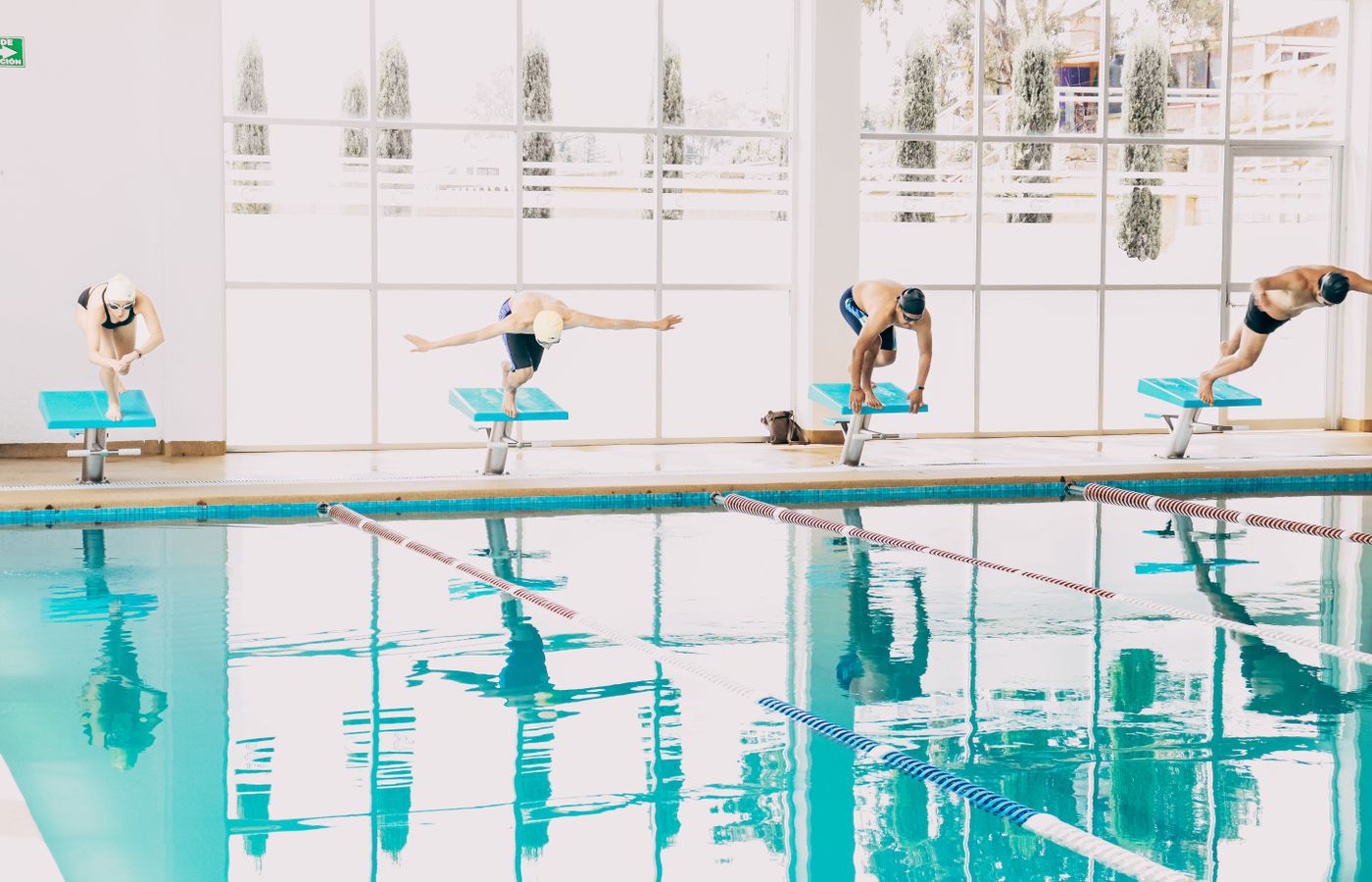 Swimmers poised on diving boards, ready to dive into an indoor pool during training.