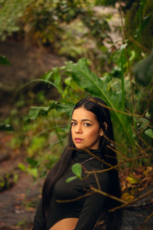 Free Elegant portrait of a woman in black, surrounded by vibrant green foliage, in a rural setting. Stock Photo