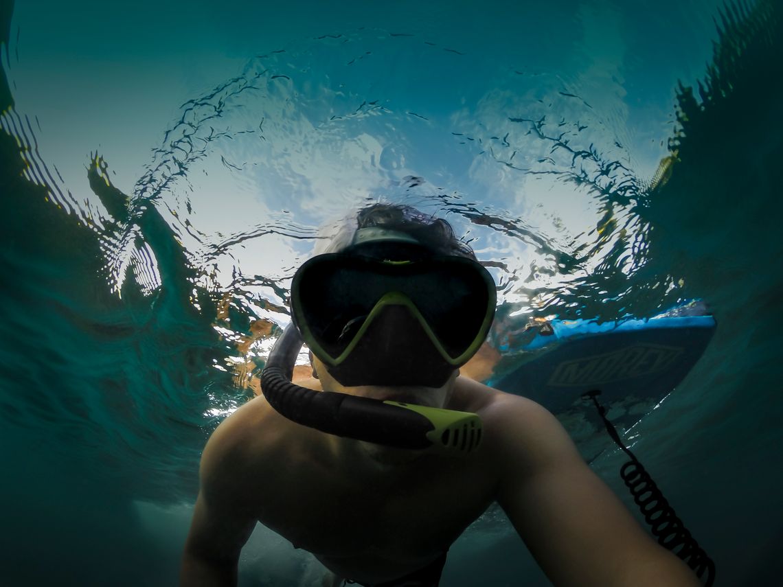 A snorkeler wearing a mask in clear water near a paddle board