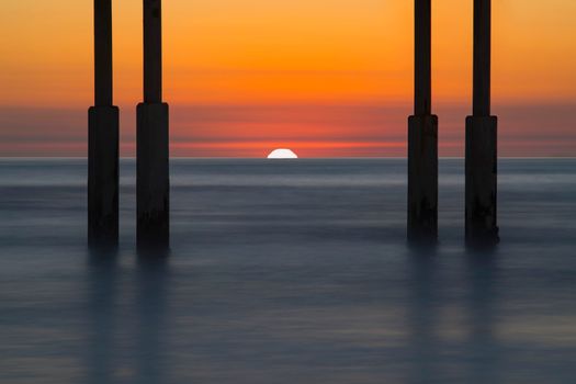 Sunset view through pier pillars with calm sea and vibrant sky.