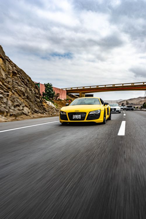 Free Dynamic shot of a yellow sports car driving on an open rural road under a cloudy sky. Stock Photo
