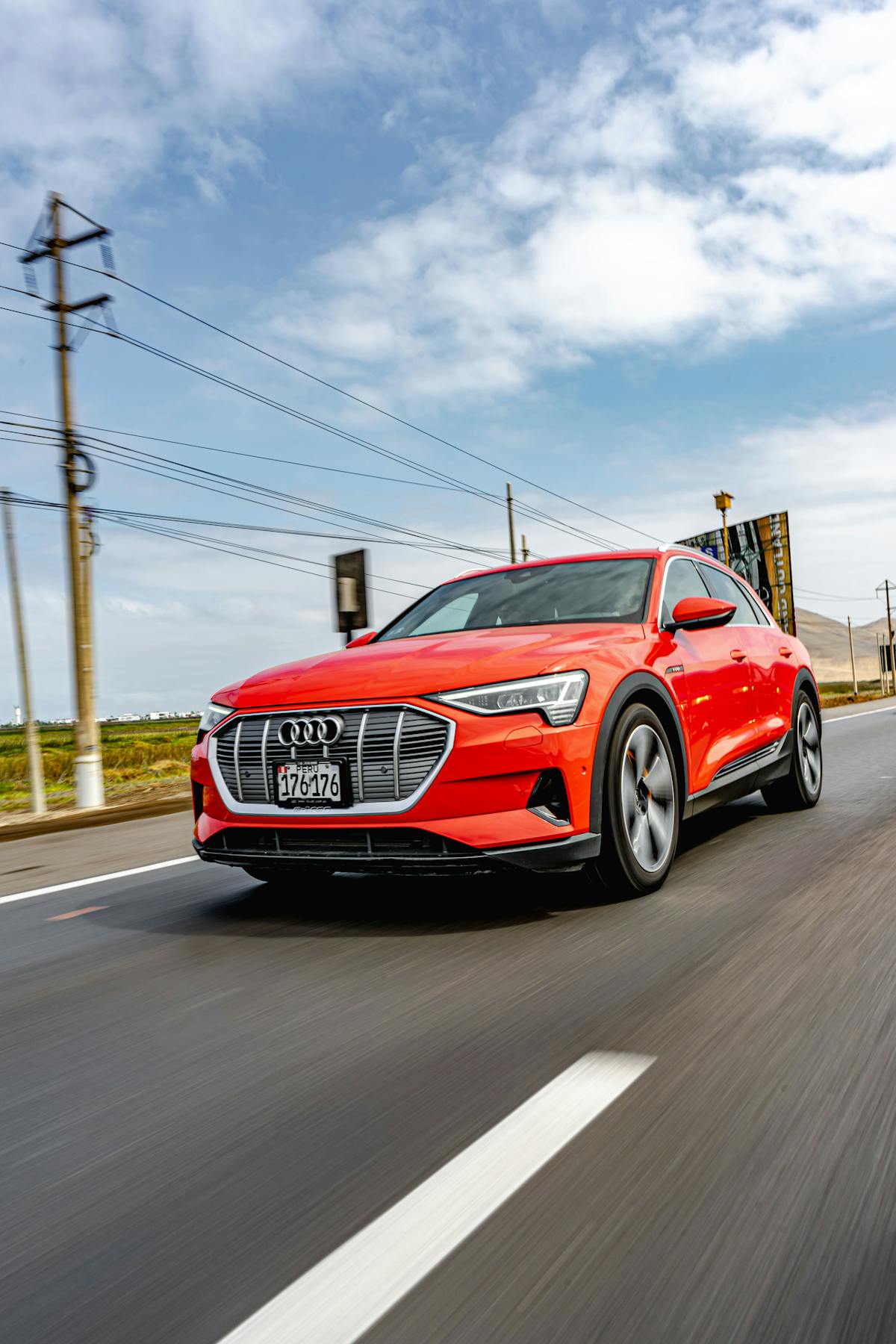 Red electric Audi E-Tron SUV driving on an open rural highway under blue sky during a road trip