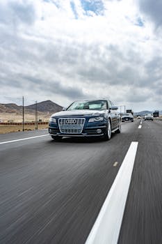 A high-speed shot of cars driving on a desert highway with mountains and cloudy skies in the background.