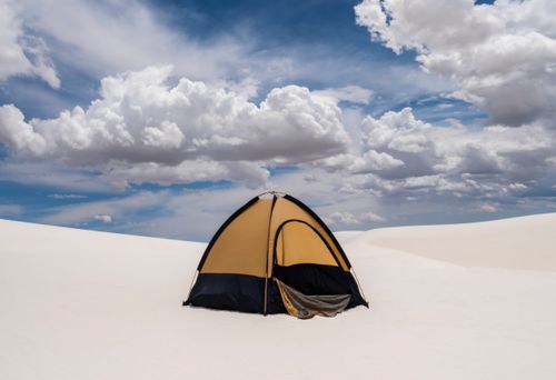 Free A solitary tent in a tranquil desert landscape beneath dramatic clouds, offering a serene camping experience. Stock Photo
