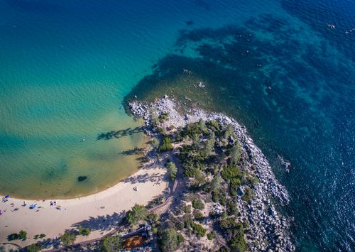 Free Explore a captivating aerial view of an unspoiled beach bordered by crystal-clear ocean waters and lush greenery. Stock Photo
