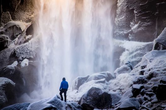 Lone hiker explores a snowy landscape with a majestic waterfall backdrop.