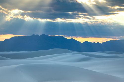 Free Beautiful desert scene with sunbeams breaking through clouds over dunes and distant mountains. Stock Photo