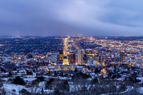 Free A breathtaking aerial view of a city illuminated at dusk during winter, showcasing urban lights and snow-covered buildings. Stock Photo