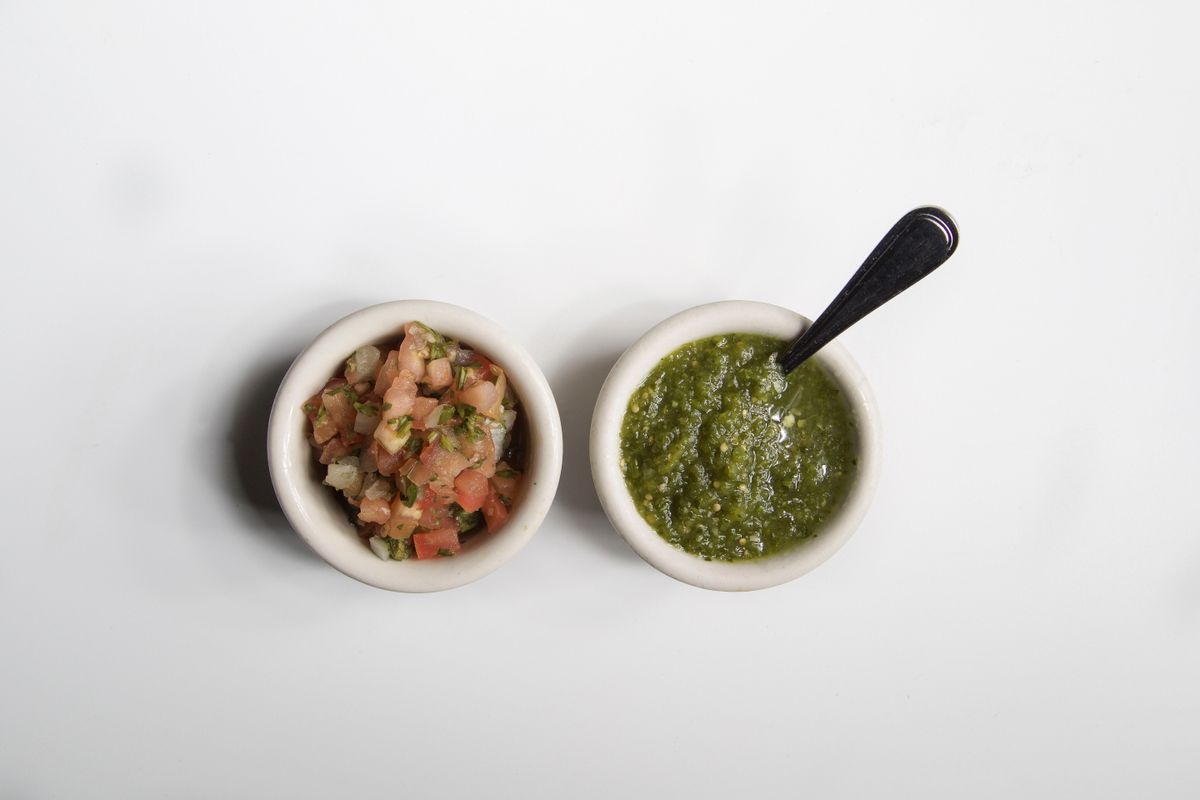 Two small white bowls, one with chunky pico de gallo and one with smooth green salsa