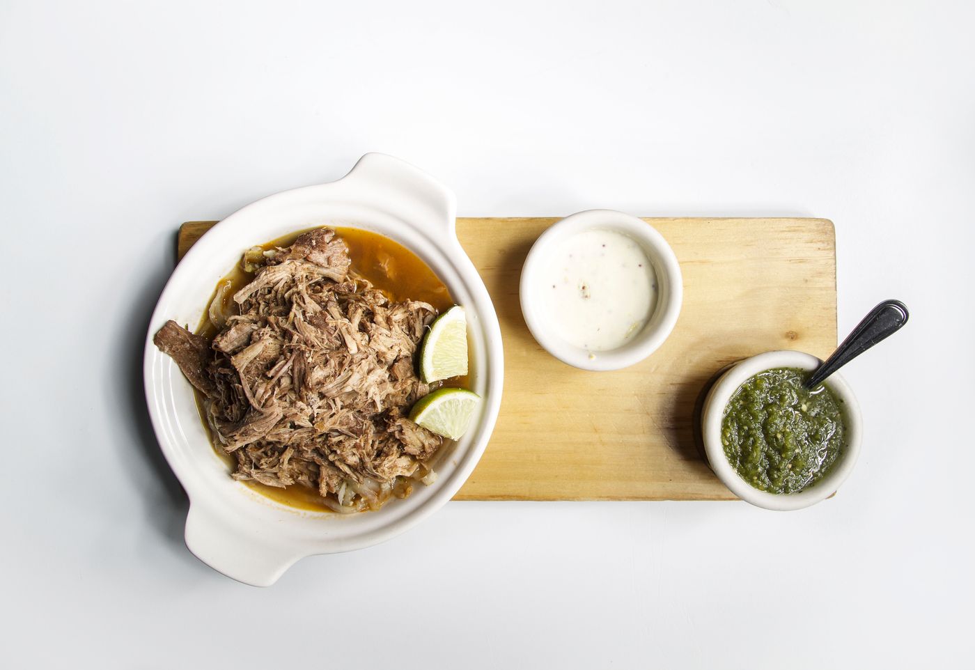 Top view of shredded meat with lime and sauces on a wooden platter, perfect for food presentations.
