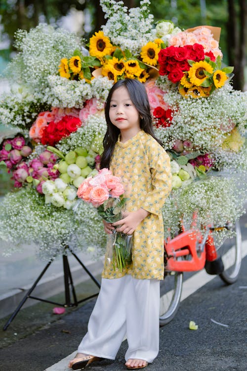 Little Girl in Yellow Dress Posing by a Heap of Flower Bouquets