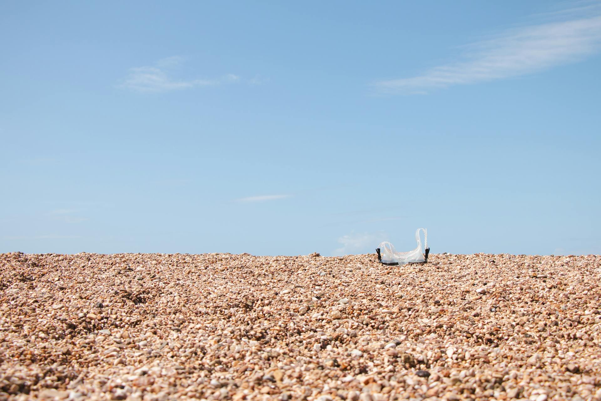 A plastic bag on a sunlit pebble beach in Vlorë County, Albania. Bright and evocative of environmental themes.