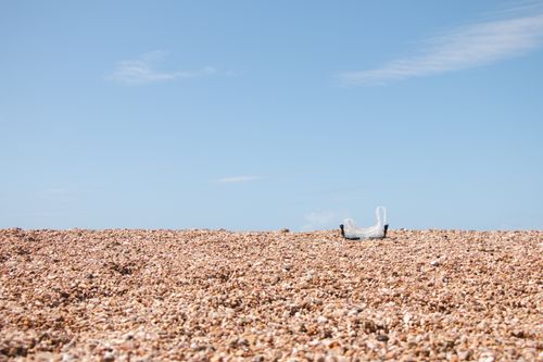 Free A plastic bag on a sunlit pebble beach in Vlorë County, Albania. Bright and evocative of environmental themes. Stock Photo