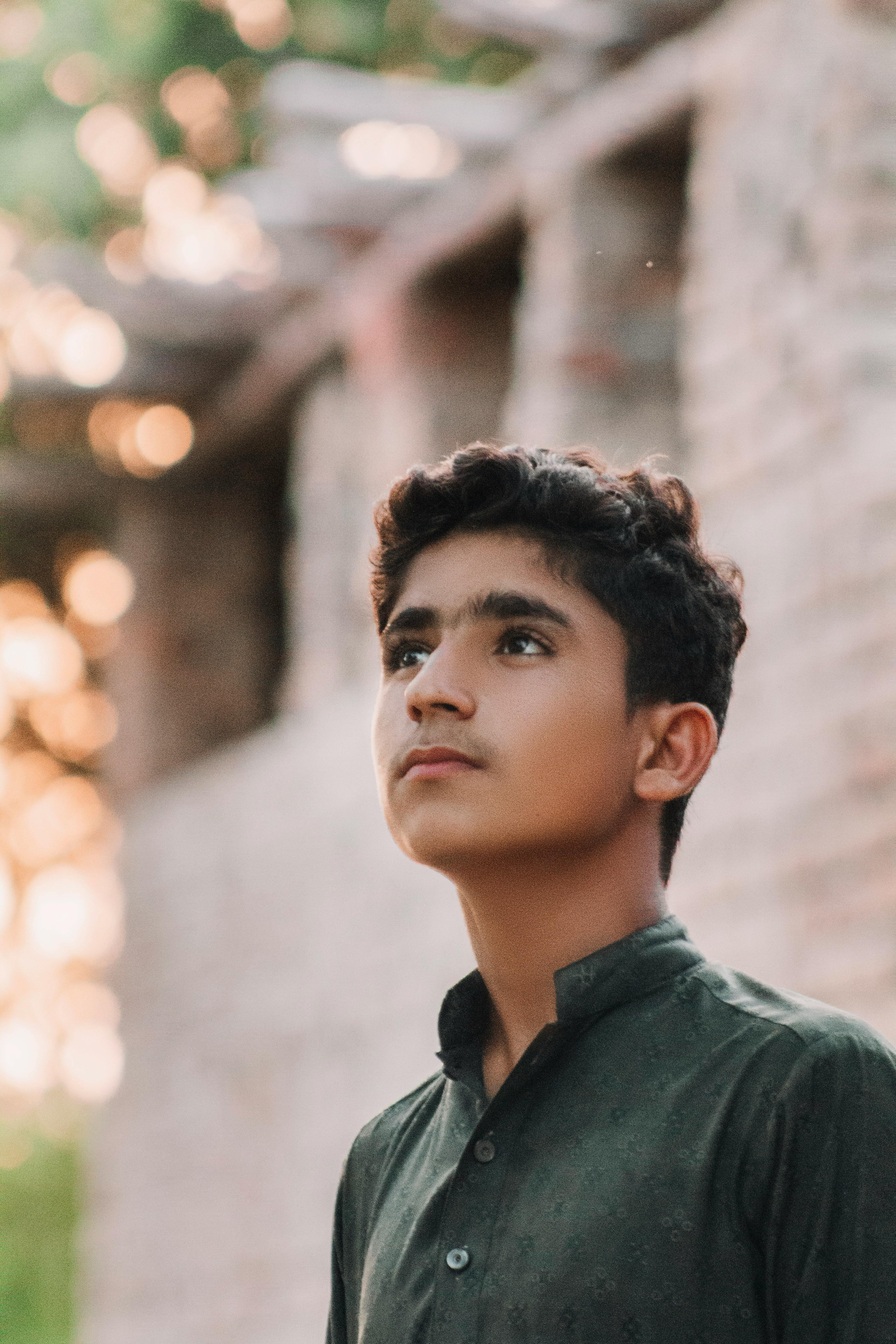 Portrait of a young man in a green shirt, posing outdoors next to a brick wall.