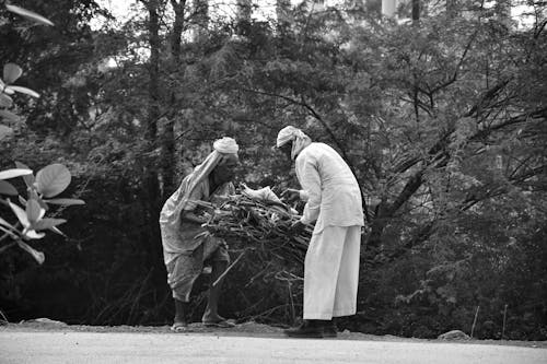 Two Elderly Men in Traditional Clothing Tying Up a Bundle of Brushwood