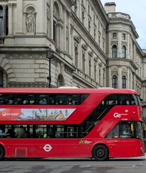 Classic red double-decker bus passing historic architecture on a London street, symbolizing urban travel.