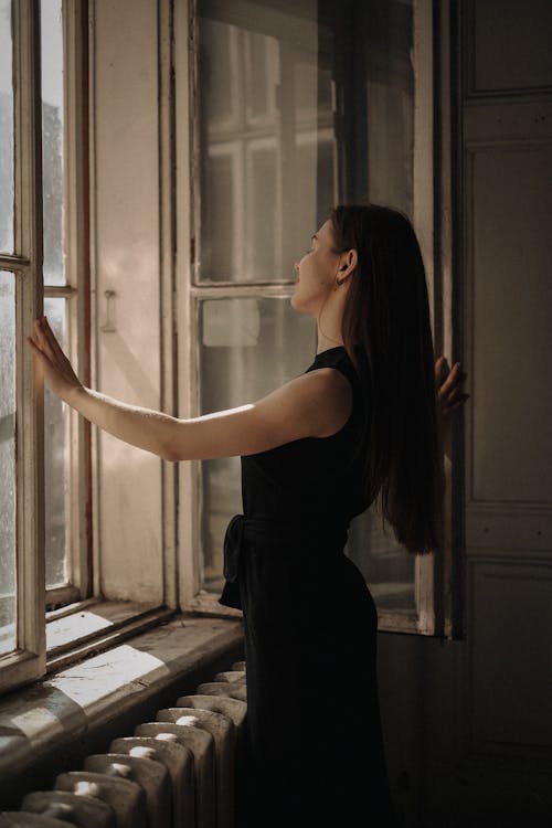 Woman in a Black Dress Standing in front of a Window