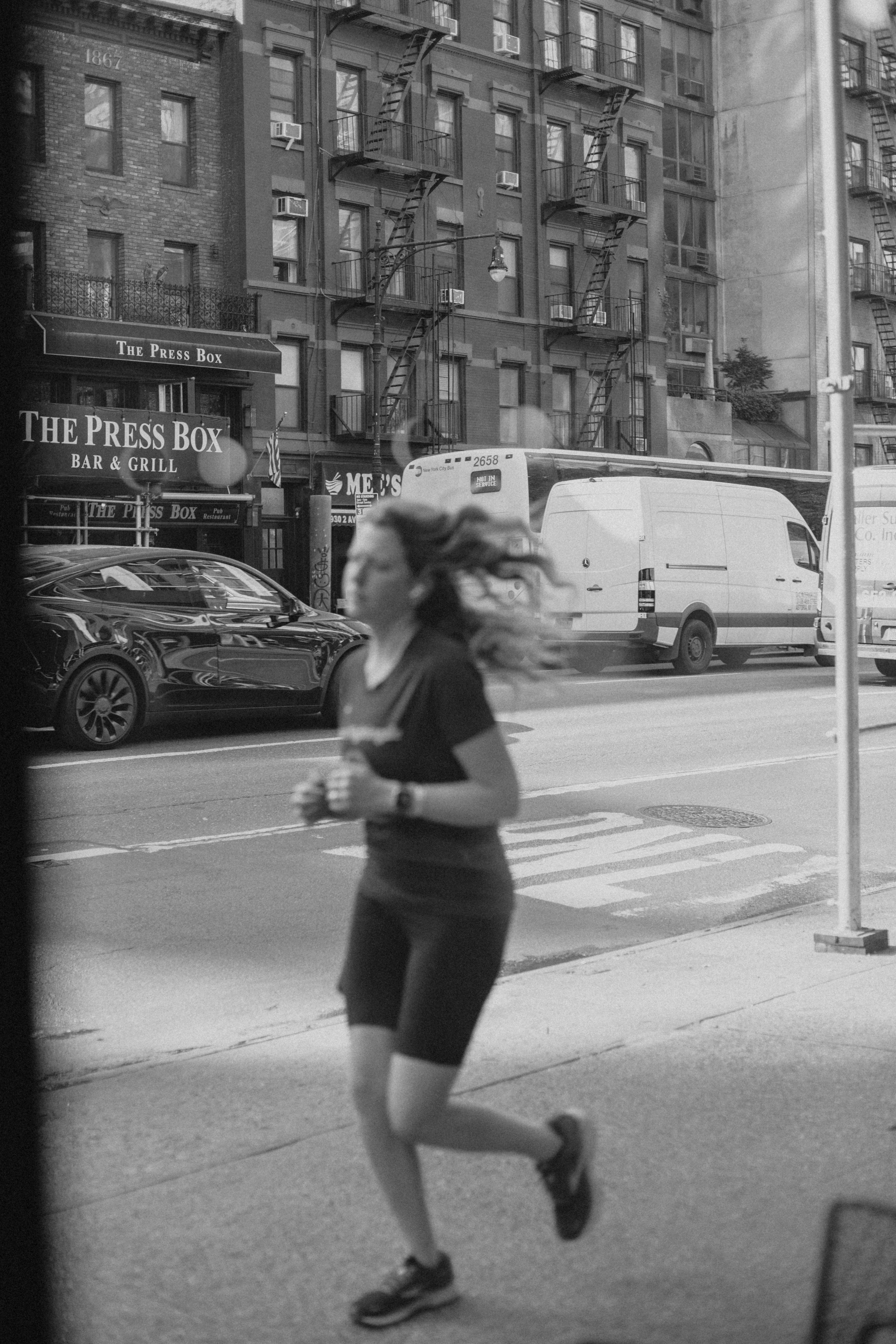 Grayscale image of a woman jogging along a bustling street in New York City.