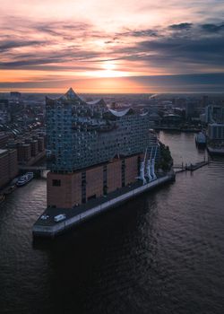 Stunning drone shot of Elbphilharmonie in Hamburg during a vibrant sunset over the river.