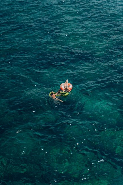 Two women enjoying a relaxing float in the ocean, captured from above on a sunny day.