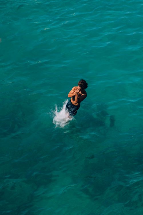 Free An adventurous man making a splash as he dives into the clear blue ocean, capturing the essence of summer fun. Stock Photo