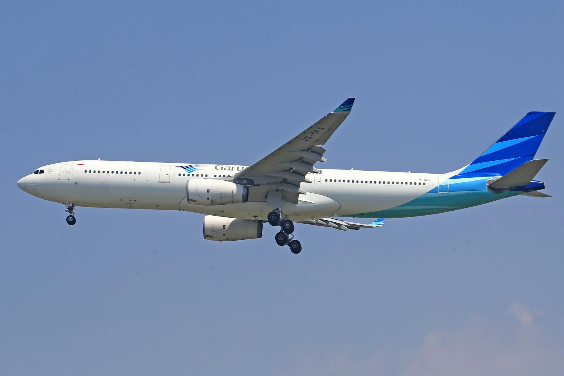 A commercial airliner flying against a clear blue sky, displaying its wing and engine details.