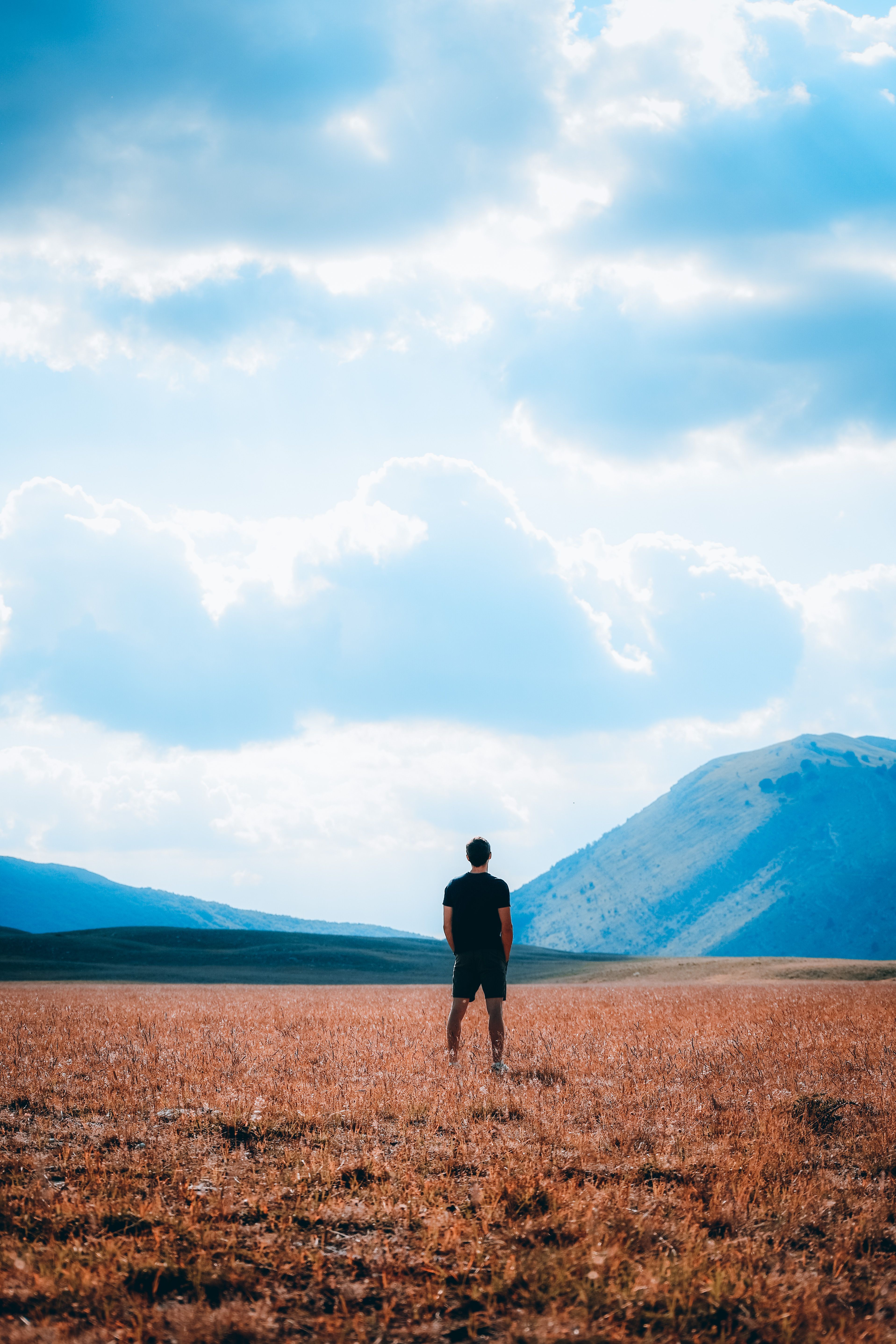 Man Standing on Grassland with Hill behind · Free Stock Photo