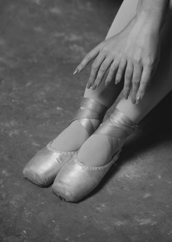 A close-up of a ballerina's feet in pointe shoes and hands on a textured floor.