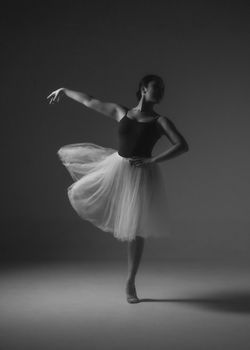 Black and white photo of a graceful ballerina posing elegantly in a studio.